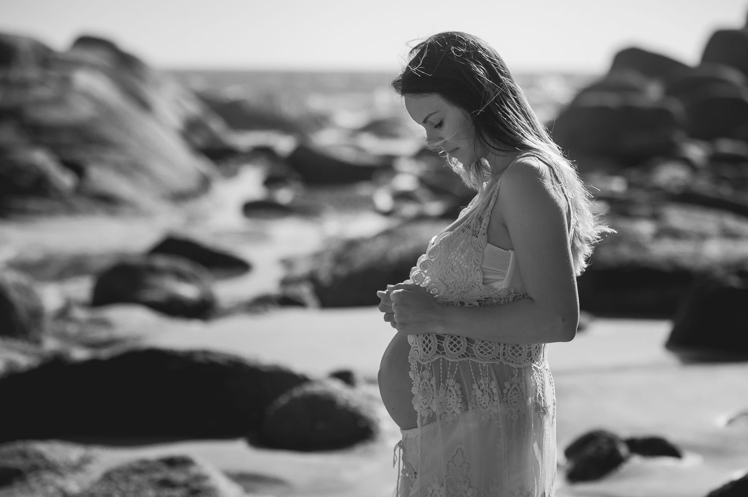 A maternity photo taken on a rocky beach with waves in the background.