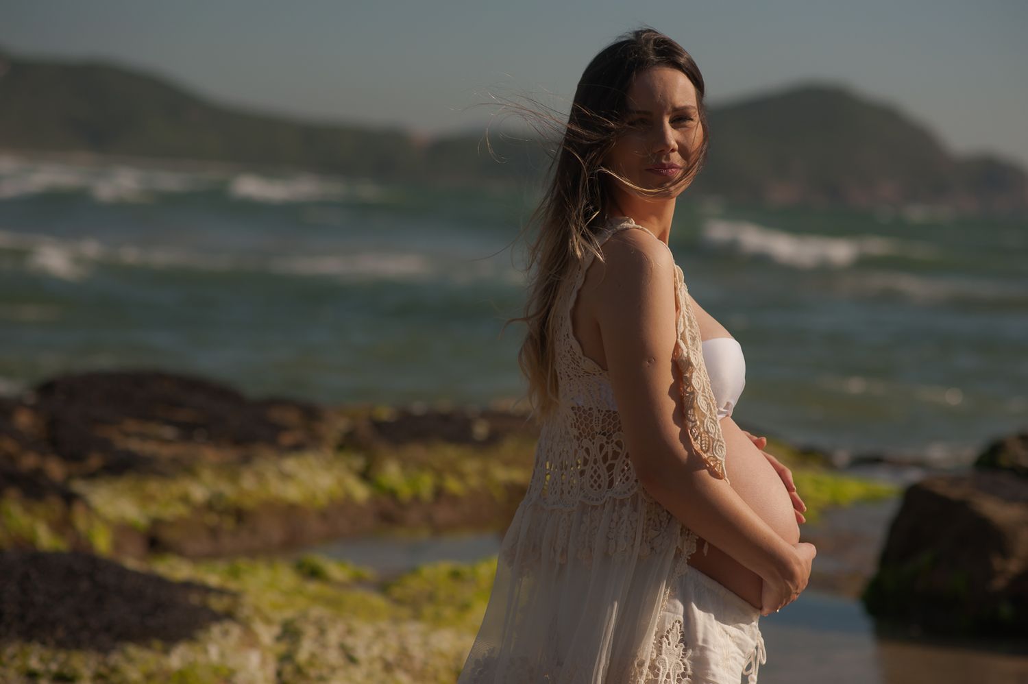 A maternity photo featuring a flowing dress against a dramatic coastal landscape.
