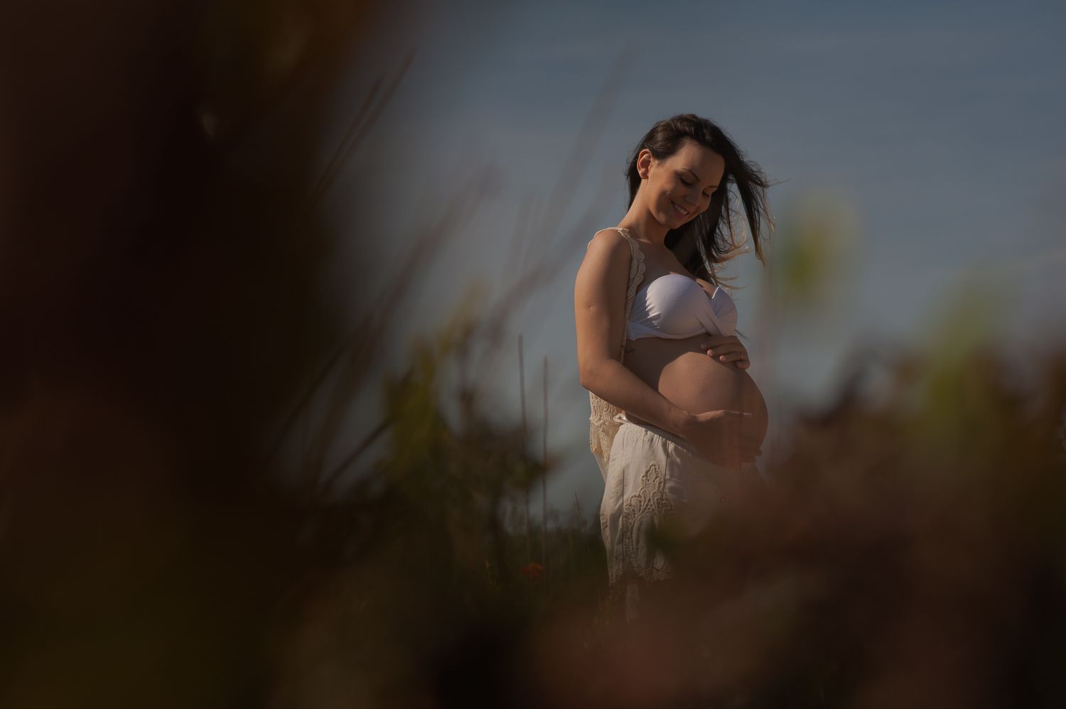 Silhouette of an expectant mother standing against a soft-focus natural background.