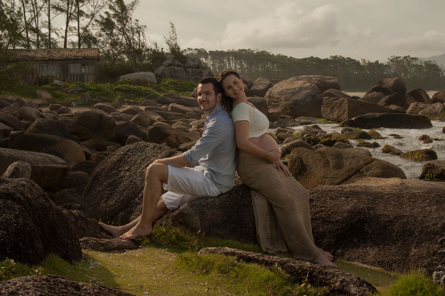 A couple resting against coastal rocks during sunset with ocean waves in the background.