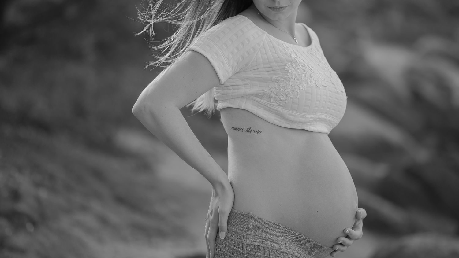 A silhouette of a pregnant belly captured in black and white against a rocky landscape.