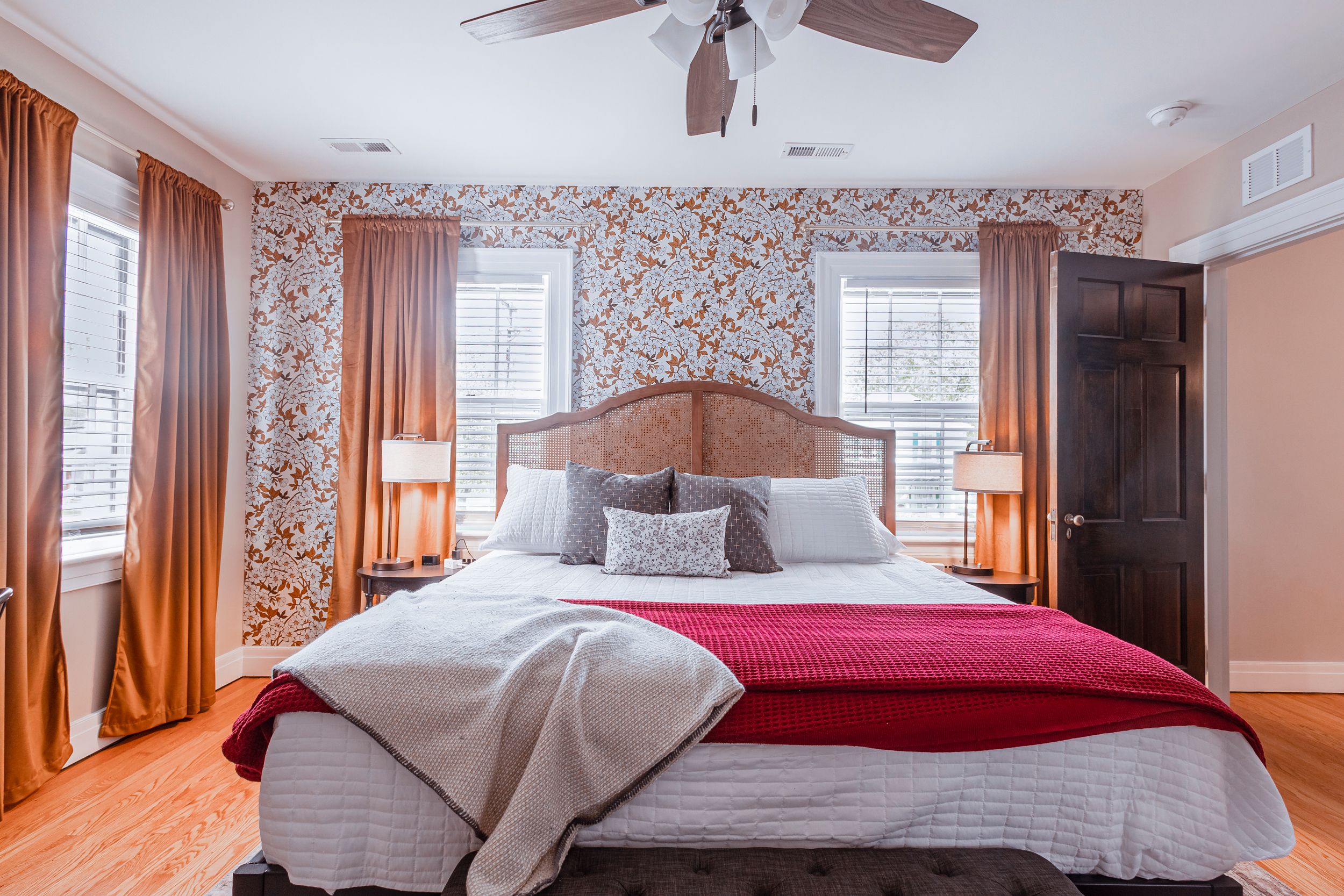 Elegant bedroom featuring floral wallpaper, coral drapes, and upholstered headboard with matching bedding.