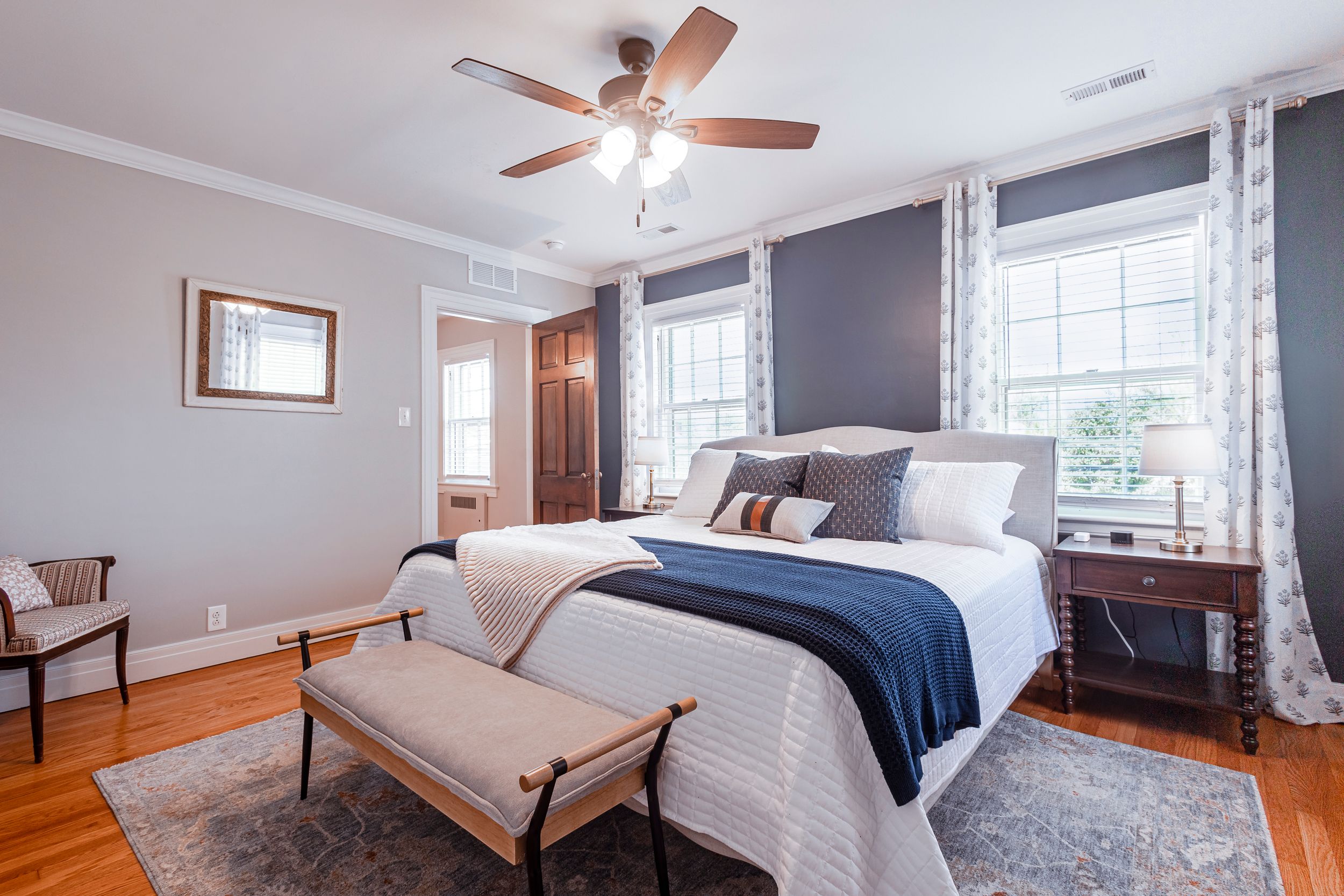 Modern bedroom with gray walls, white curtains, and navy bedding accented by a beige chaise lounge.