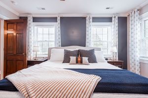 Contemporary bedroom with navy accent wall, white drapes, and striped throw blanket on king bed.