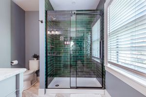 Luxurious bathroom featuring emerald green subway tile shower with glass doors and natural lighting.