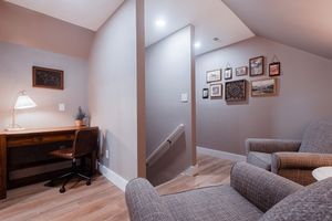 Modern home office nook with desk and seating area featuring gray walls and wood flooring.