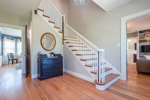 Elegant entryway with wooden staircase, hardwood floors, and navy blue dresser beneath a round gold mirror.