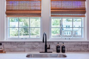 Modern kitchen window with bamboo shades, white marble countertop, and matte black faucet.