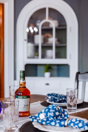 Dining room detail with arched window, blue napkins, and bourbon bottle on wooden table.