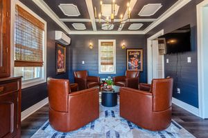 Elegant sitting room with navy walls, coffered ceiling, and four brown leather swivel chairs around a round table.