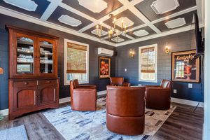 Formal room with navy walls, ornate ceiling, built-in cabinets and leather barrel chairs on patterned rug.