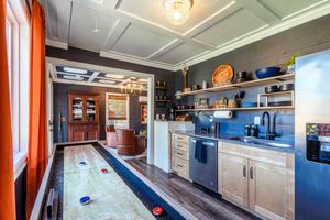 Game room featuring a shuffleboard table, blue walls, and white kitchen area with open shelving.