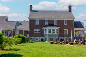 Rear view of brick colonial home with bay window and outdoor seating area.