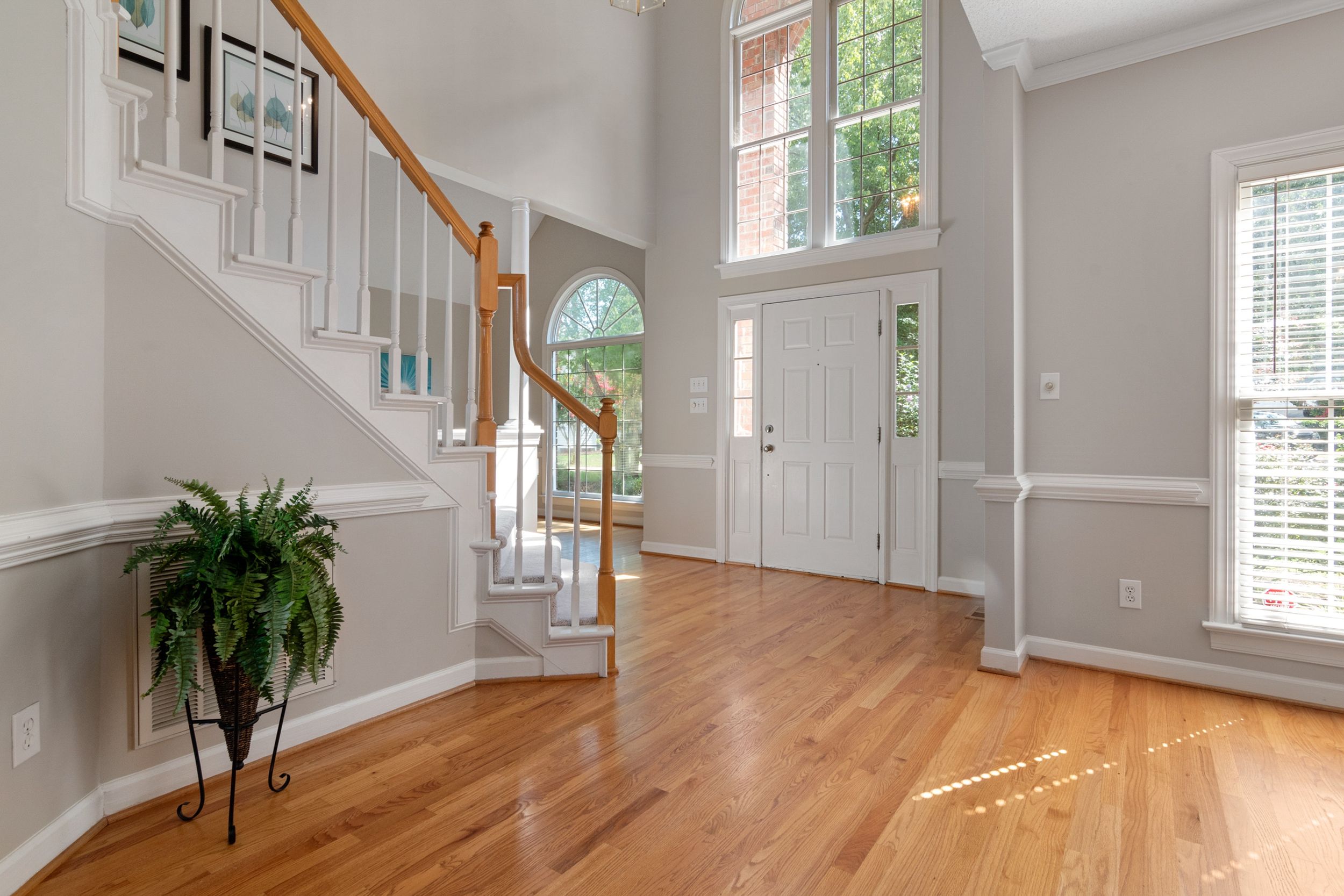 Bright entryway with hardwood floors, white walls, and elegant staircase featuring natural lighting.