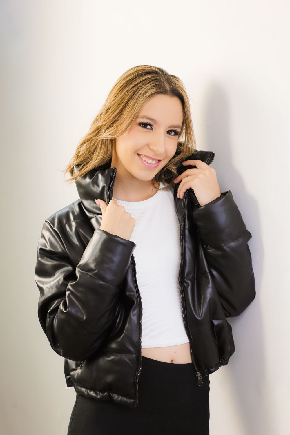 Model wearing black leather jacket and white crop top poses against white background.