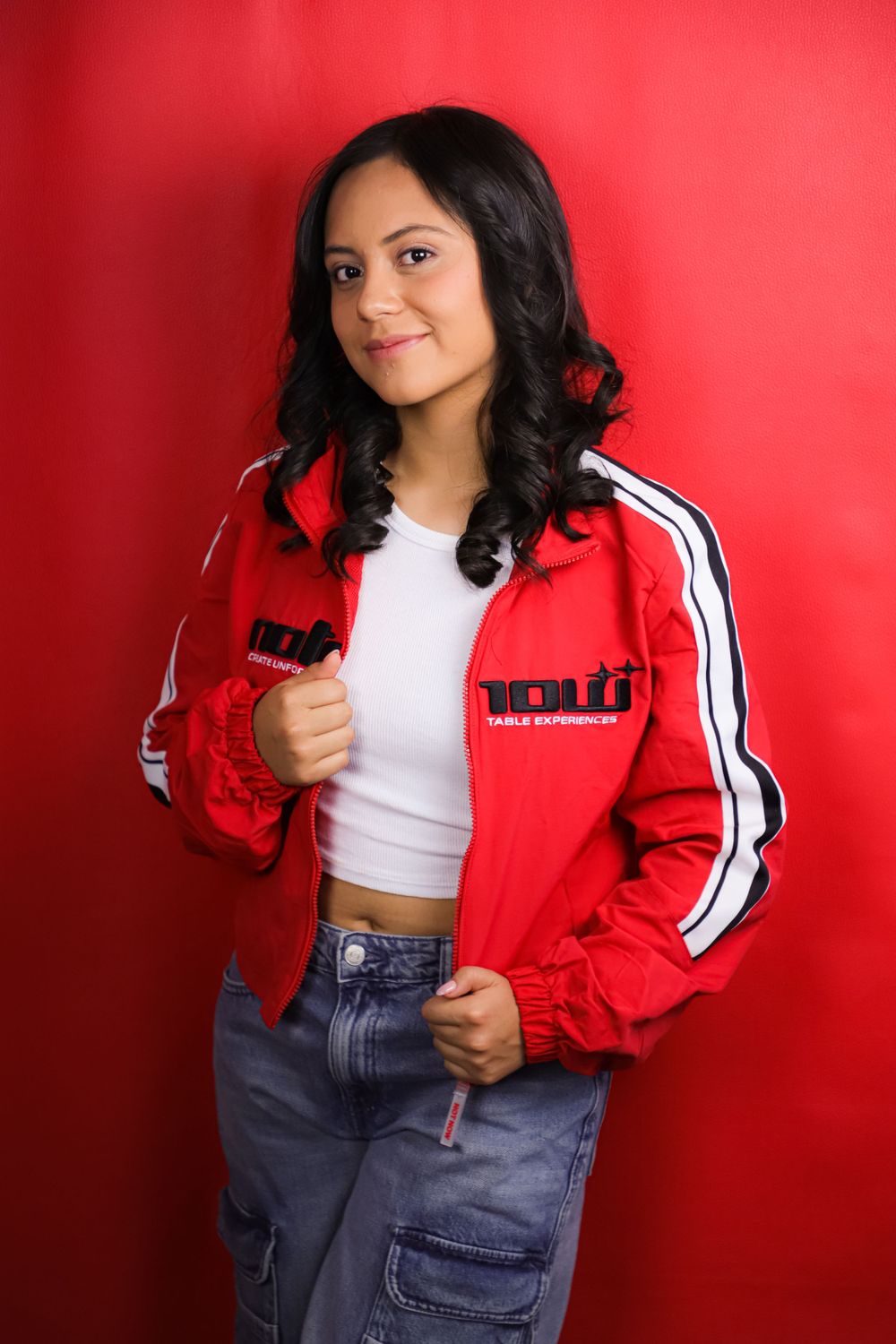 Sporty casual look with red track jacket, white top and jeans against red background.