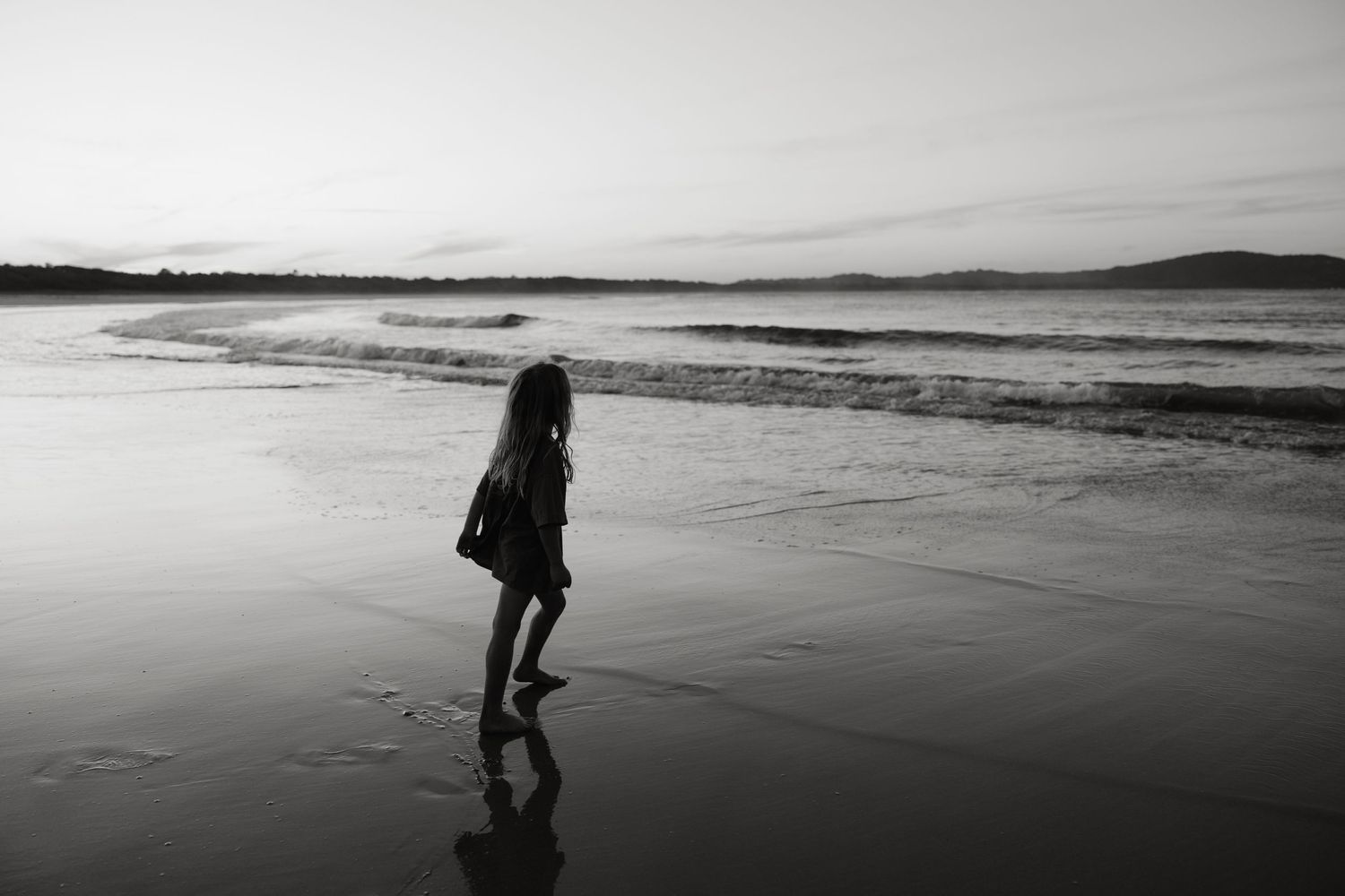 Silhouette of person walking alone on beach at sunset in black and white.