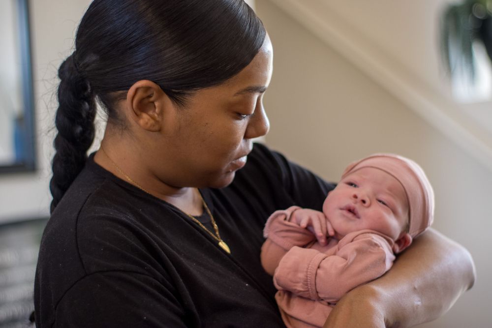 A woman tenderly holds and gazes at a newborn baby dressed in a pink outfit indoors.