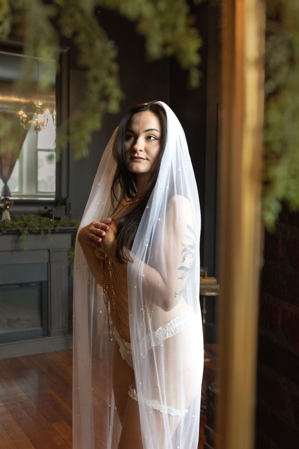Person in white veil poses elegantly by window with natural lighting.