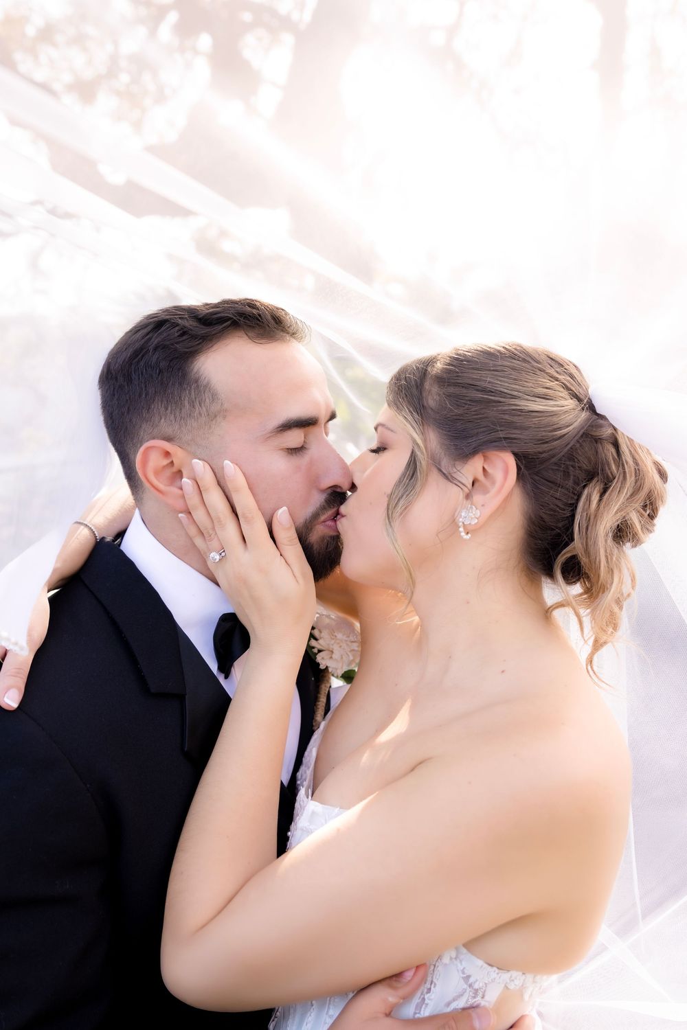Bride and groom sharing a romantic kiss under a flowing white veil on their wedding day.