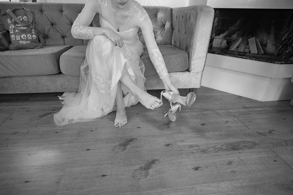 Black and white image of final wedding shoe adjustments on wooden floor.