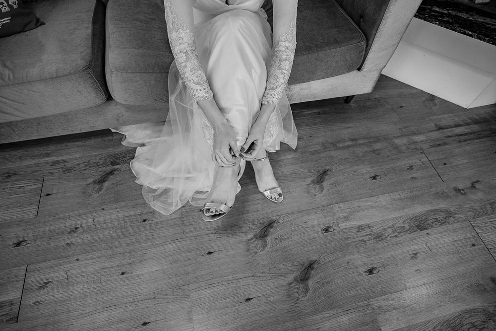 A close-up shot of a bride in white dress adjusting her shoe on wooden flooring.
