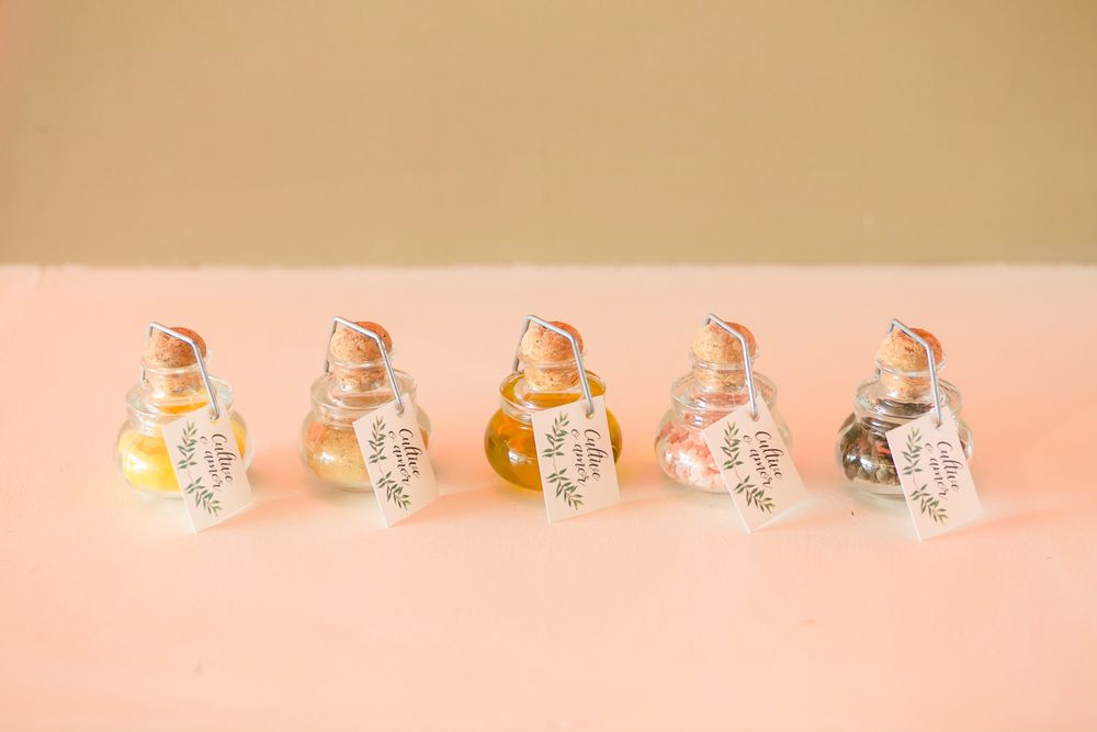 Five small favor bottles with tags arranged in a row on pink background.