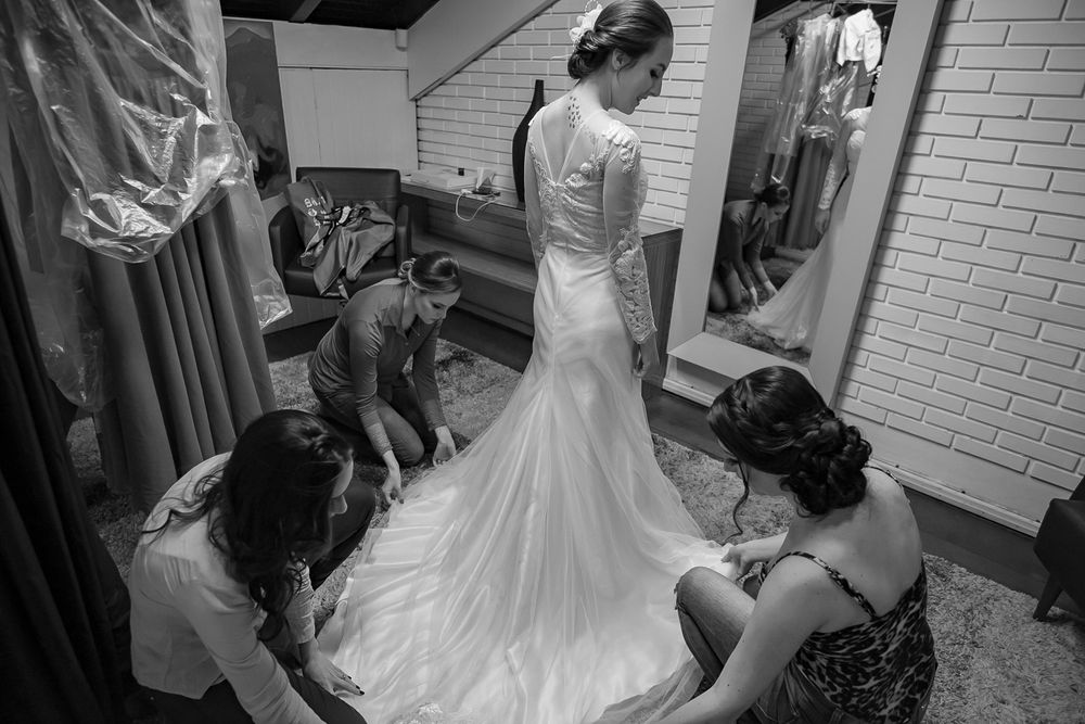 Bridesmaids helping adjust the train of a fitted wedding dress in a dressing room.