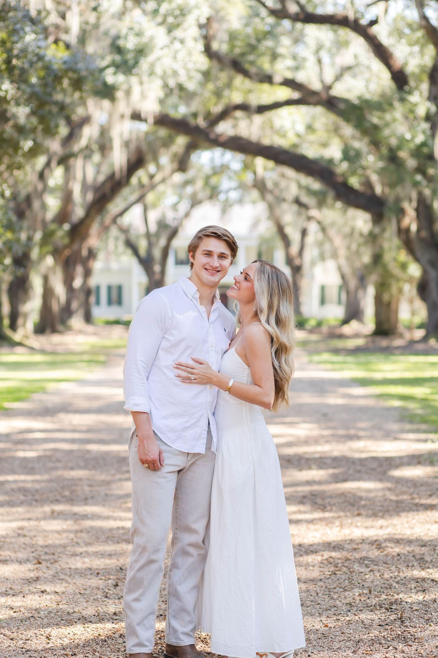 Couple in white outfits sharing a romantic moment under Spanish moss draped oak trees on a garden path.