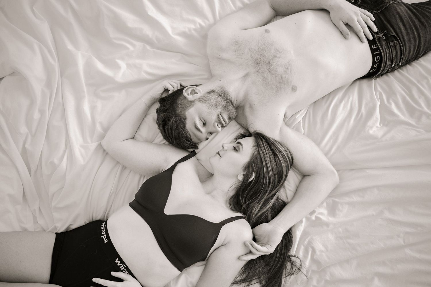 Intimate black and white portrait of two people laying on white bedding.