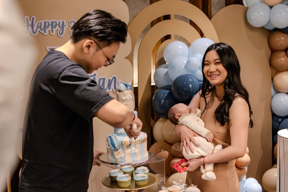 A celebration scene with cake cutting at a baby shower decorated with blue and beige balloons.
