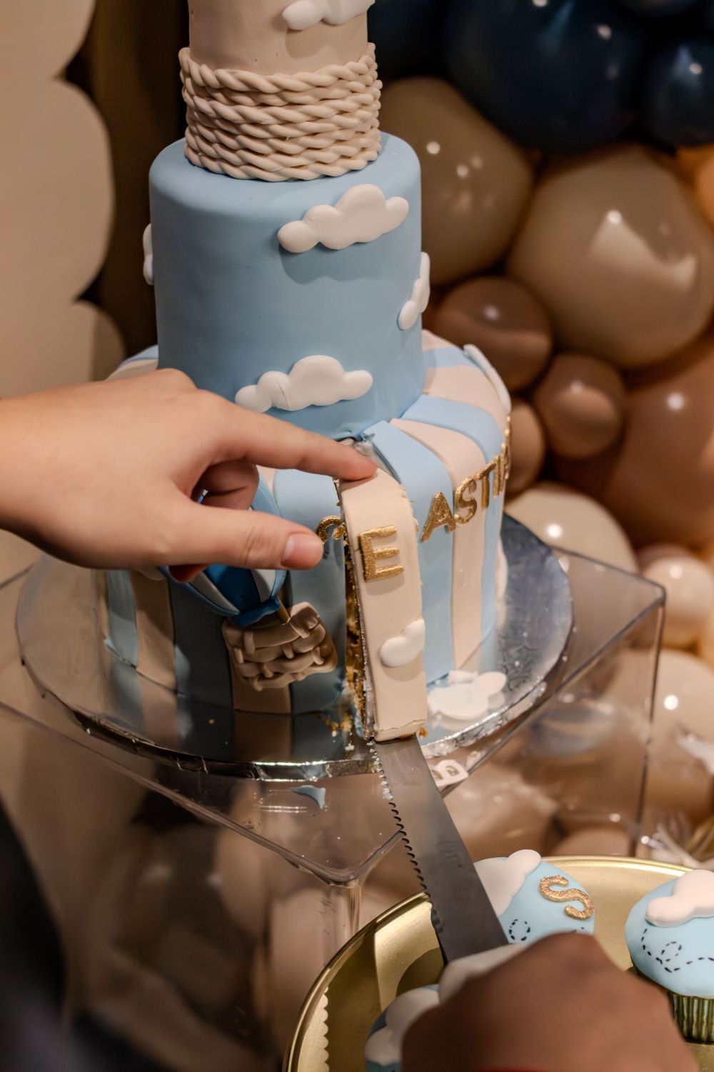 A blue and white tiered cake featuring cloud designs being cut at a celebration.