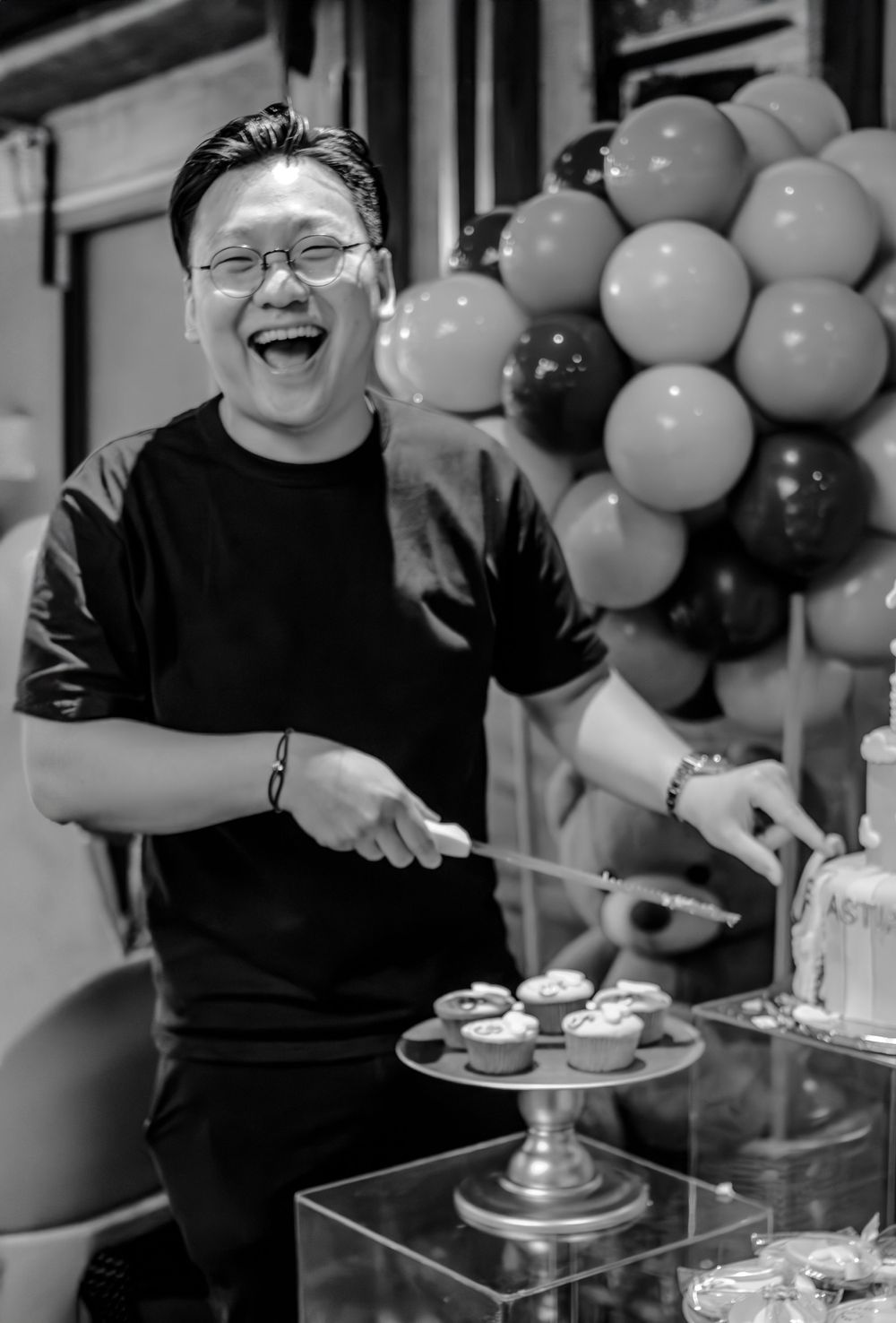 Black and white photo of person laughing while serving desserts at celebration.
