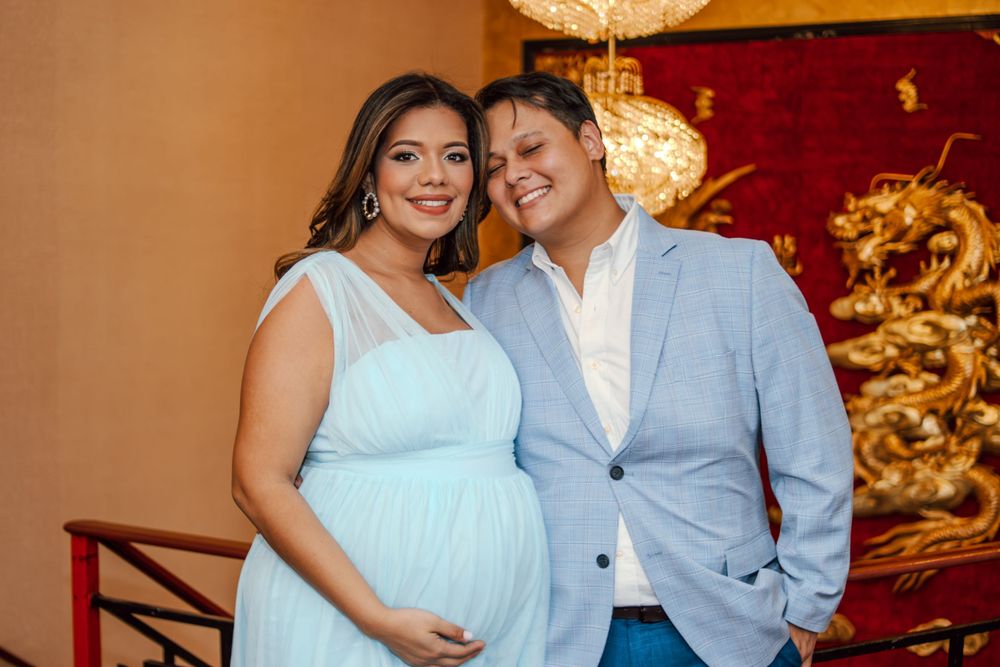 A couple in formal attire poses together in front of an ornate gold and red backdrop.