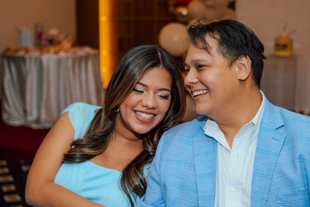 A couple in coordinated blue outfits share a tender moment at an indoor celebration.