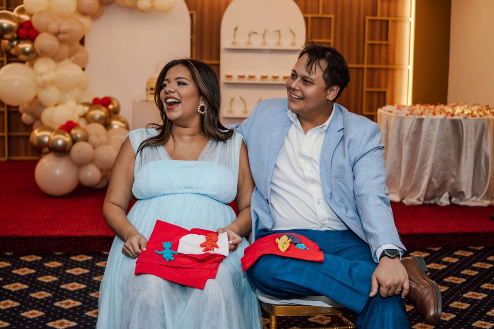 A couple shares a joyful moment while holding colorful gift boxes at a festive balloon-decorated celebration.