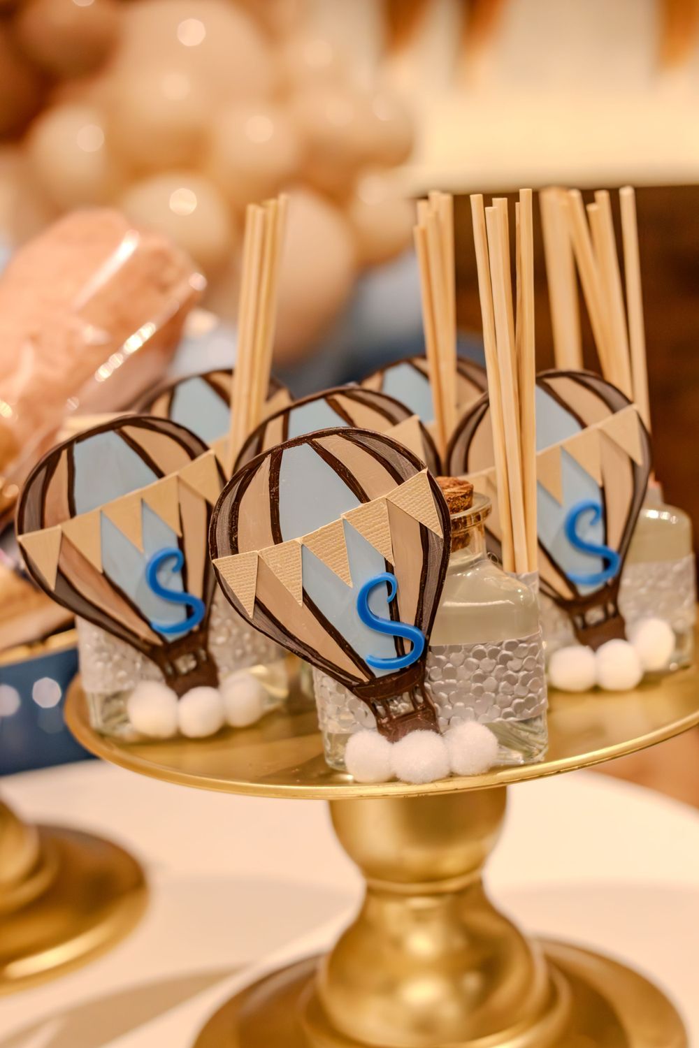 Decorated cake pops with blue and brown designs displayed on a gold cake stand.