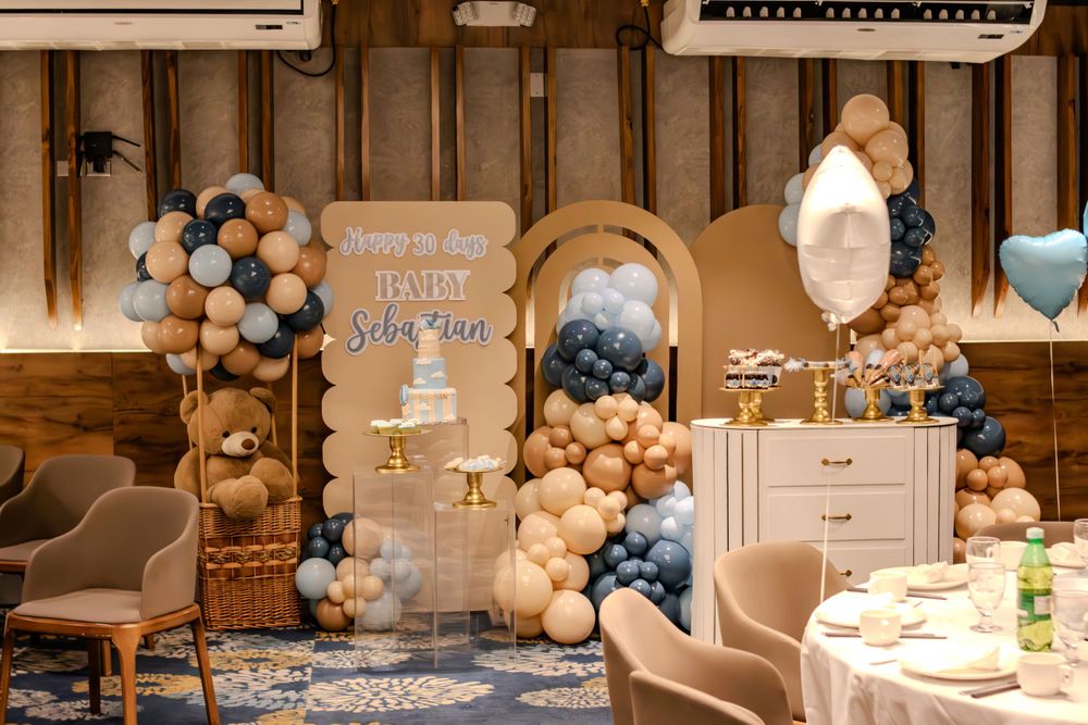 Baby shower decorations featuring blue and beige balloon arches with rustic wooden backdrops.