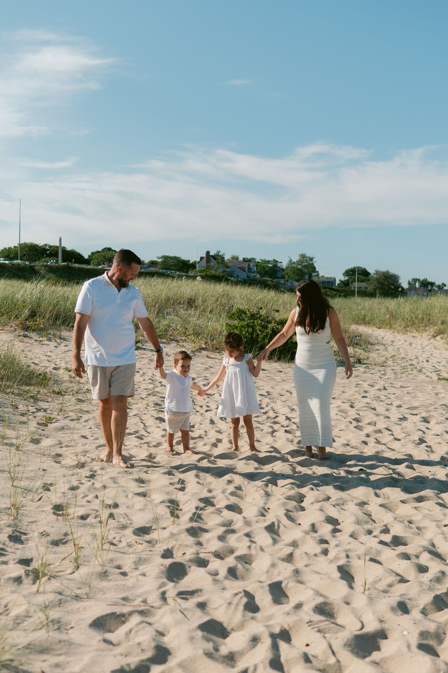 Family of four walking hand-in-hand along the water’s edge on a sunny Cape Cod beach day