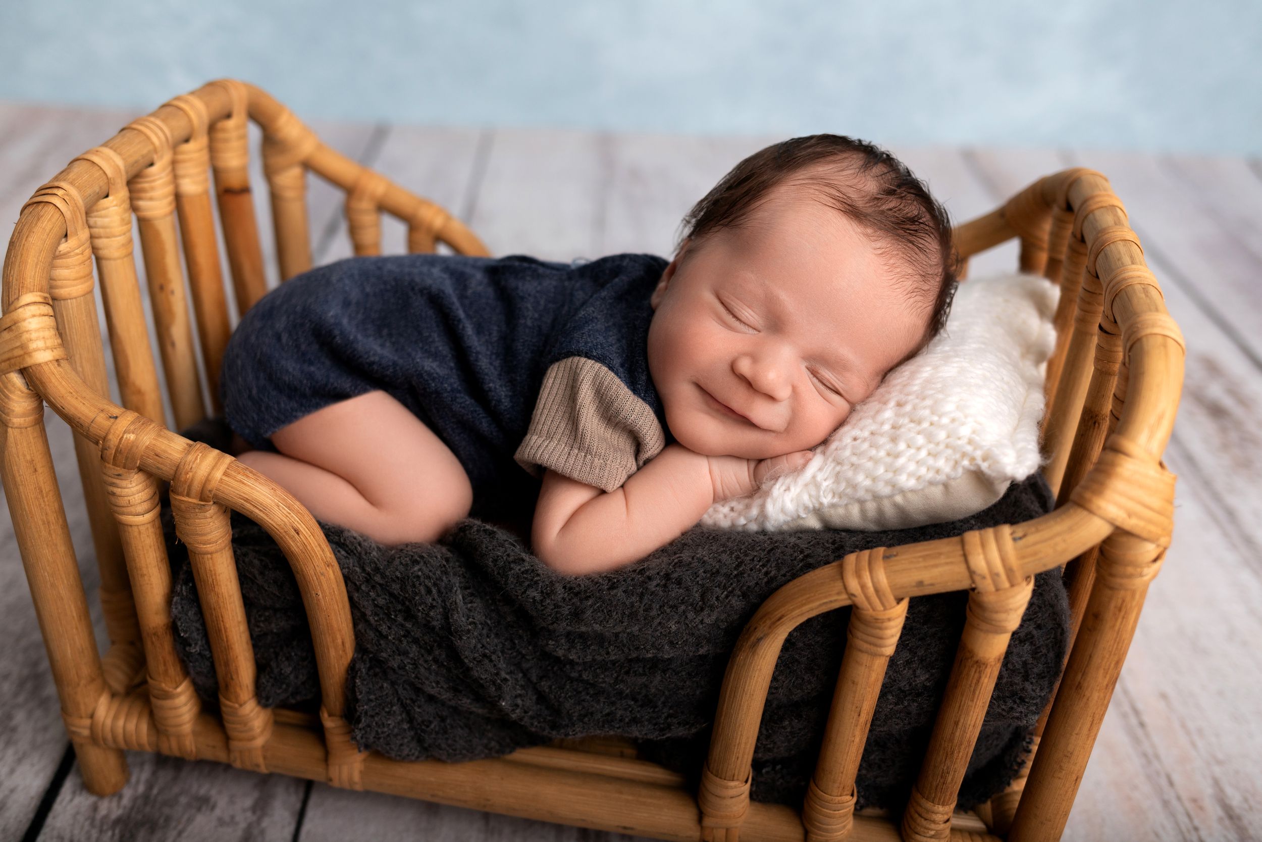 Sleeping newborn in navy outfit resting in vintage rattan bassinet.