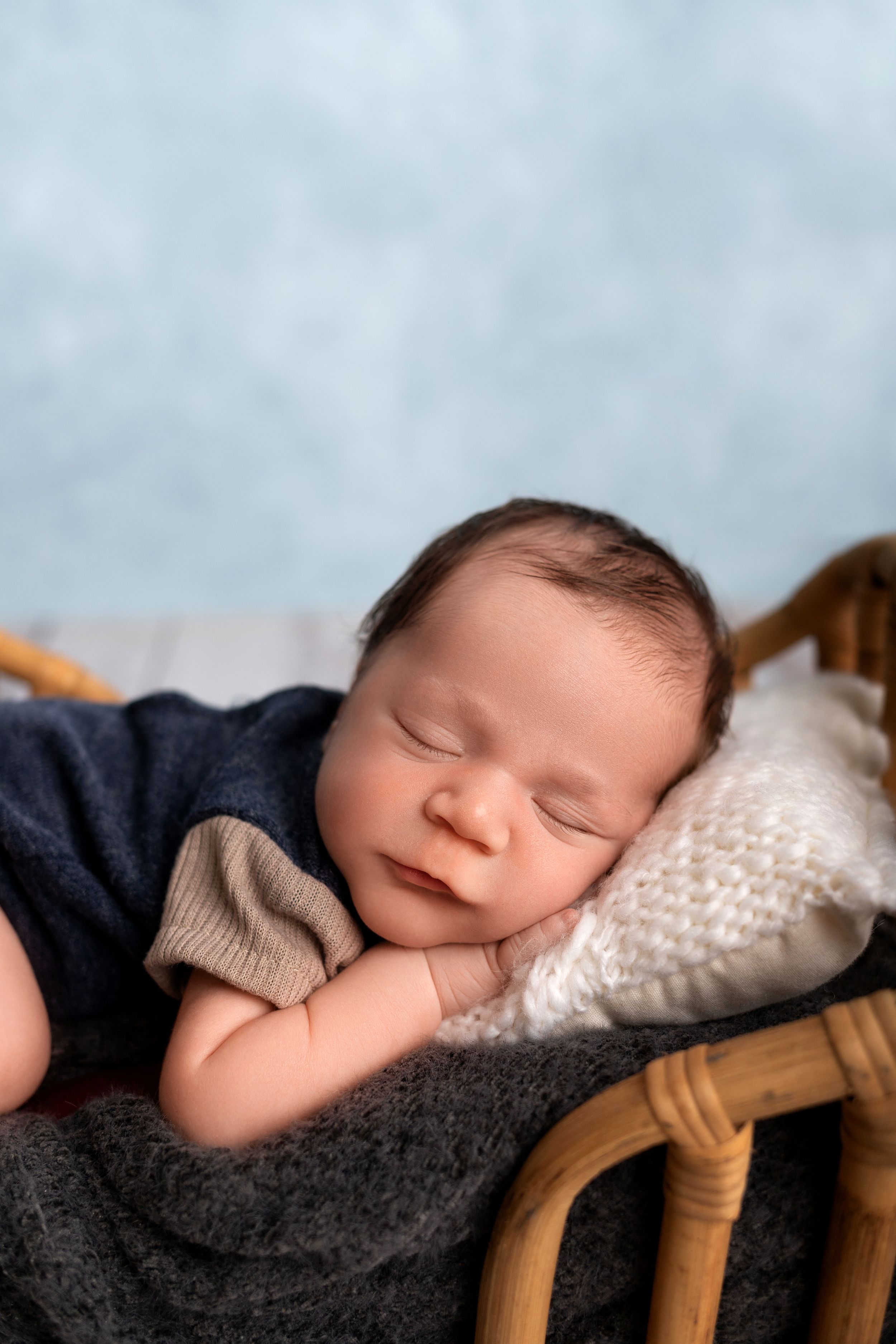 Sleeping baby in navy outfit resting peacefully in rattan bassinet.
