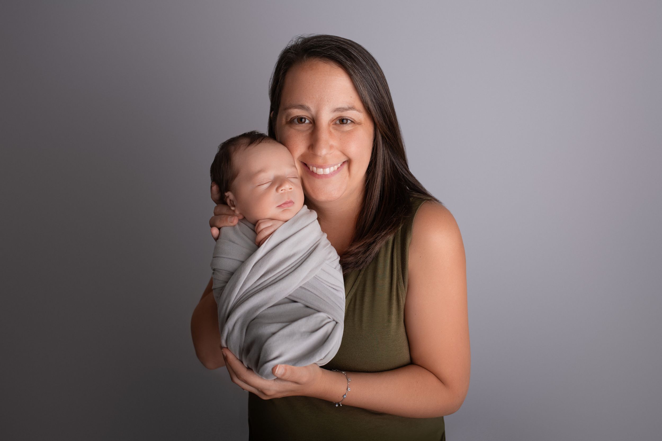 A tender moment between parent and newborn baby wrapped in soft gray fabric against a neutral background.