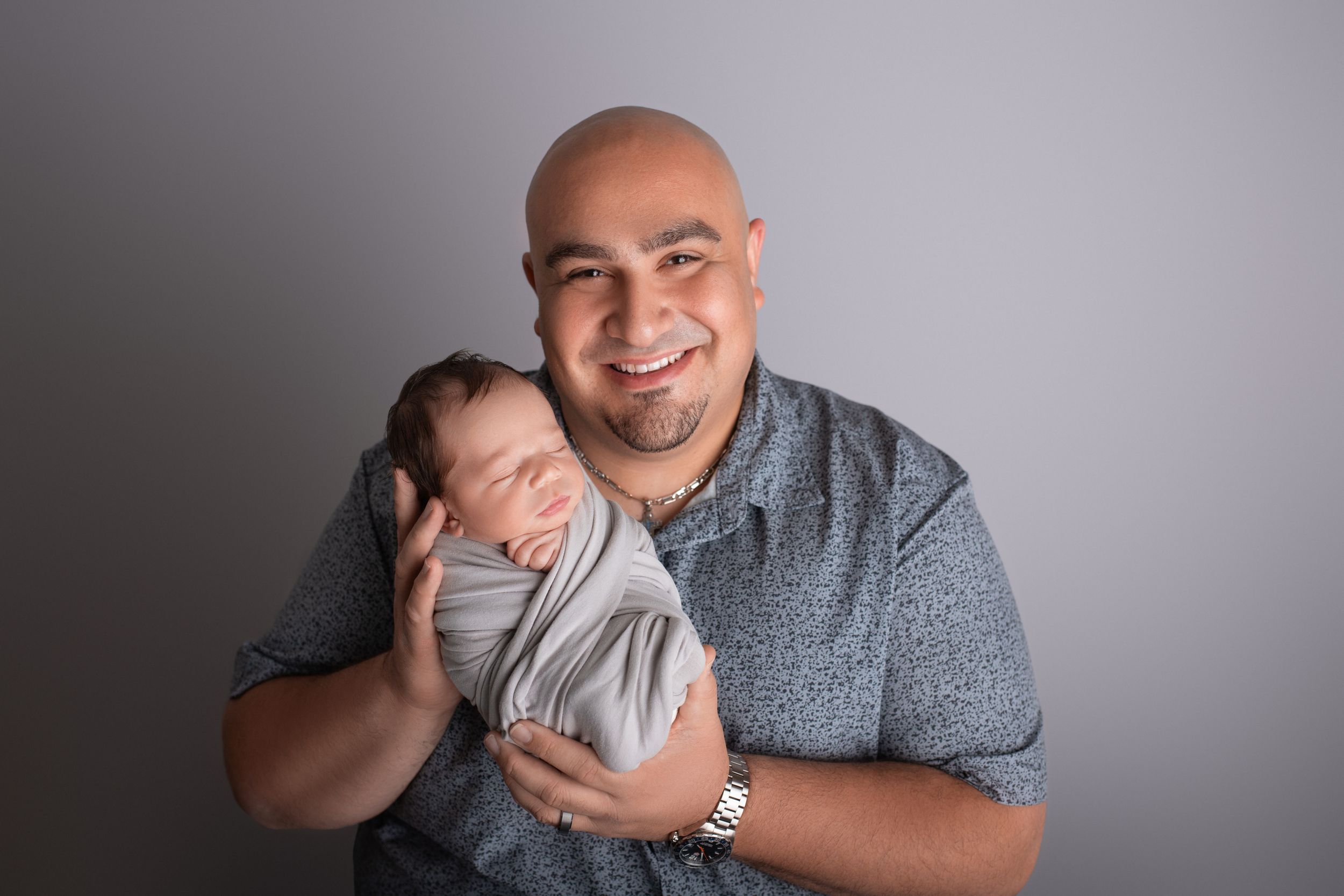 A joyful moment showing parent holding a sleeping newborn baby swaddled in gray.