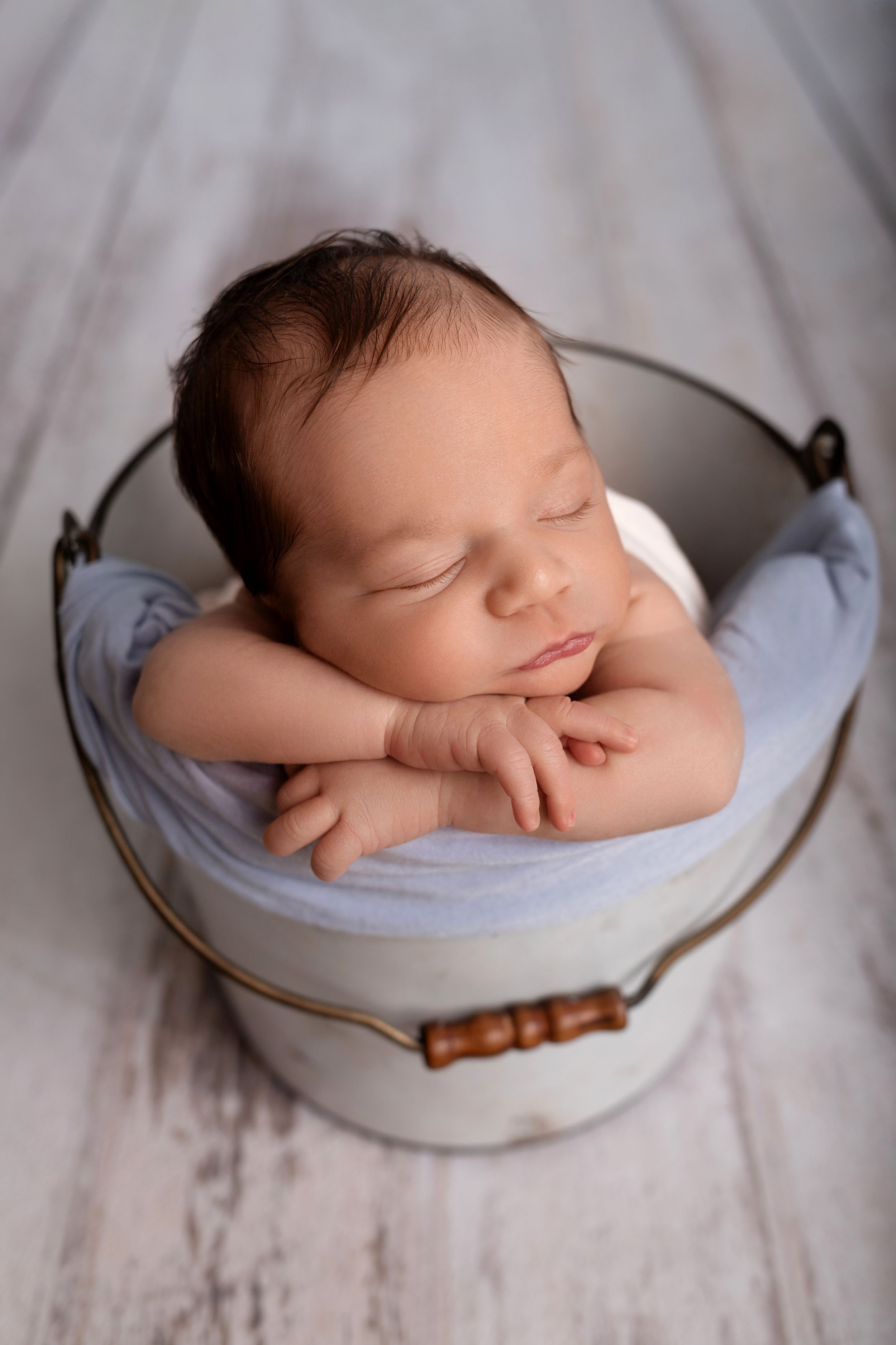 Sleeping newborn baby posed in rustic metal bucket with light blue fabric.