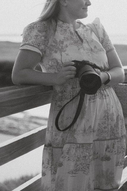 Black and white portrait of female photographer holding camera on wooden fence.