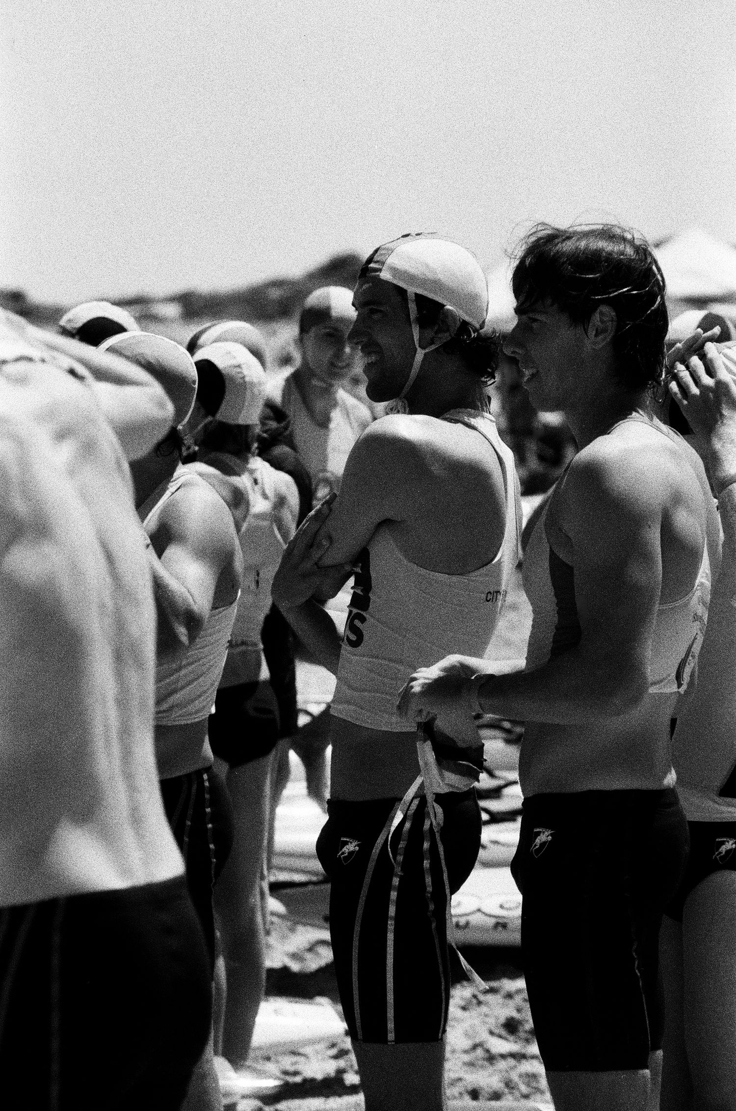 Athletes gathered at beach wearing sports attire in black and white photo.