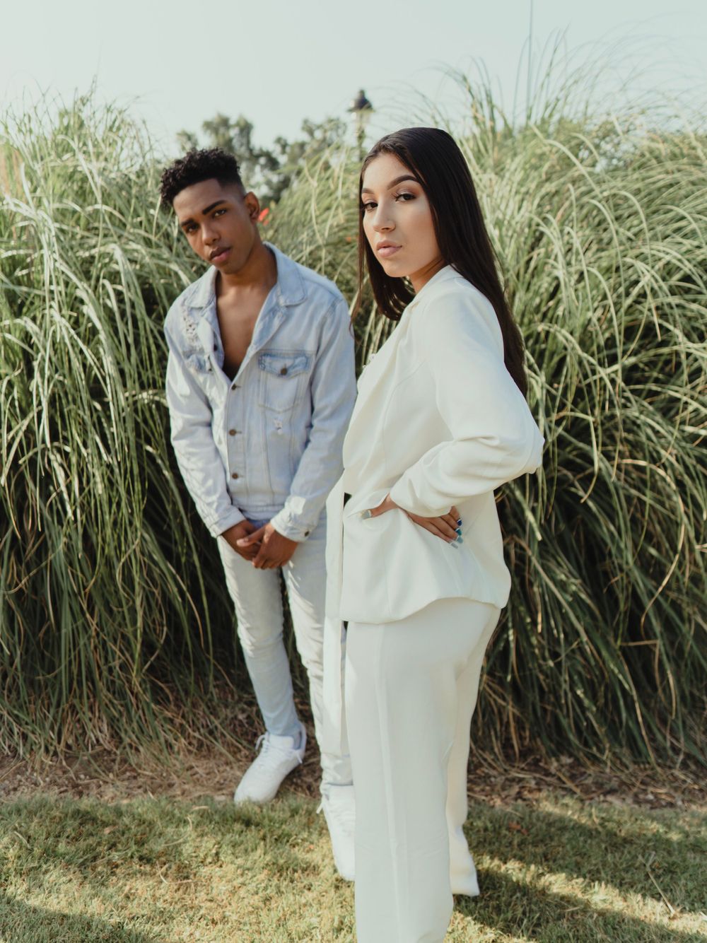 A fashion photo of two models in contrasting white and denim outfits among tall grass.