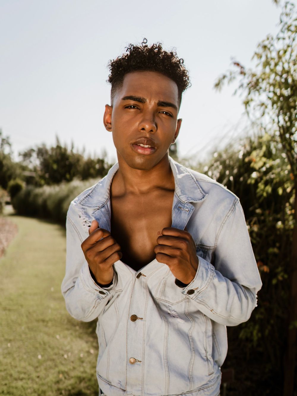A model in light denim jacket poses against natural outdoor backdrop.
