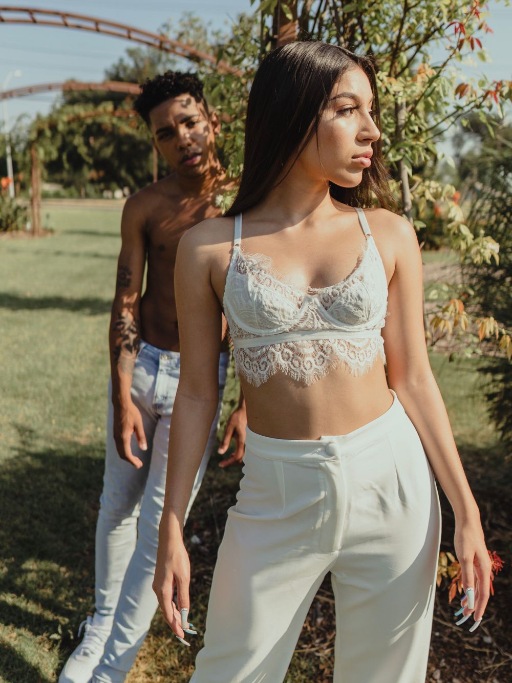 Fashion models pose in white outfits against lush garden backdrop with arched trellis.