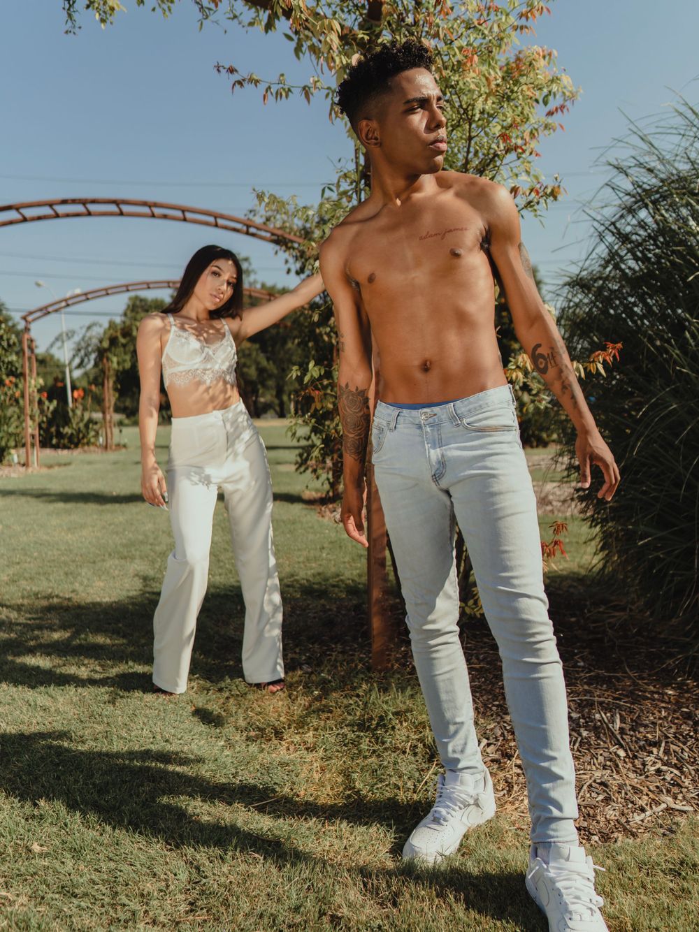 Models in coordinated white outfits strike dynamic poses in outdoor garden setting.